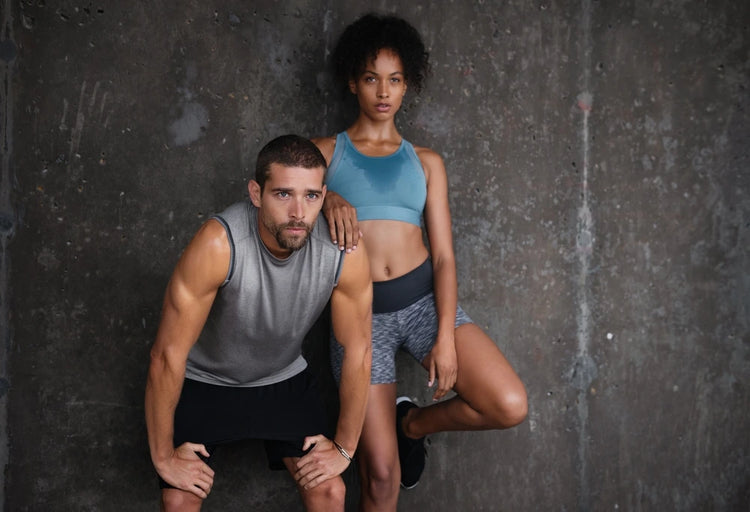 Two people in athletic wear posing against a textured dark wall.